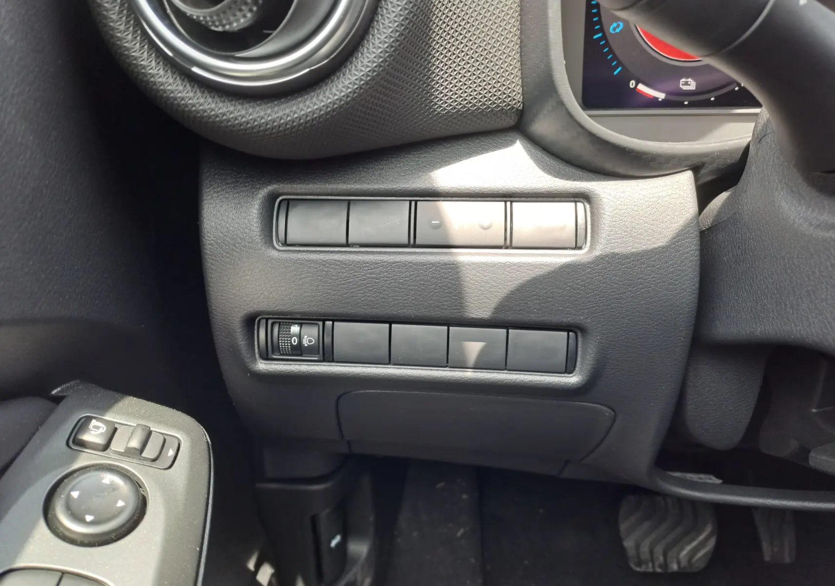 Détail intérieur côté gauche du tableau de bord du Nissan Juke Hybrid 2025 en gris squale, avec commandes et aérateur rond.