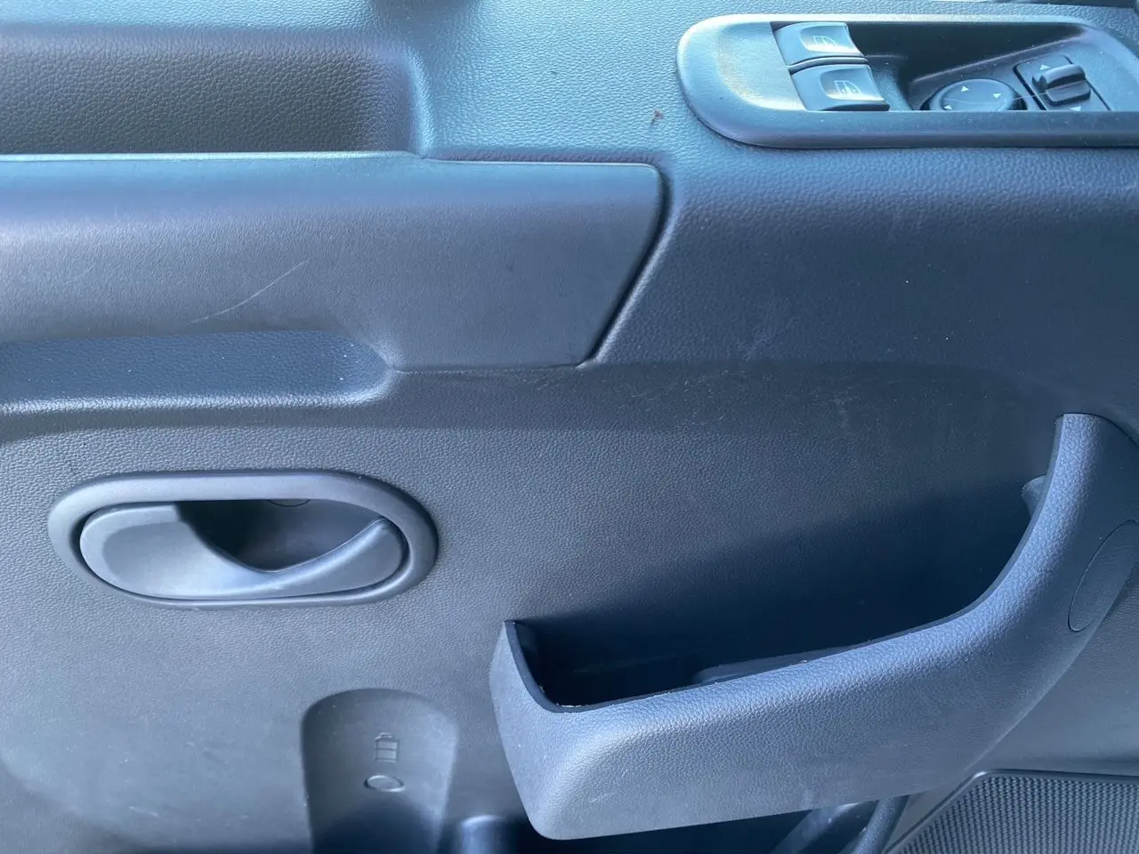 Poignée intérieure et commandes de lève-vitres côté conducteur du Renault Master Châssis Cabine 2023 en plastique noir.