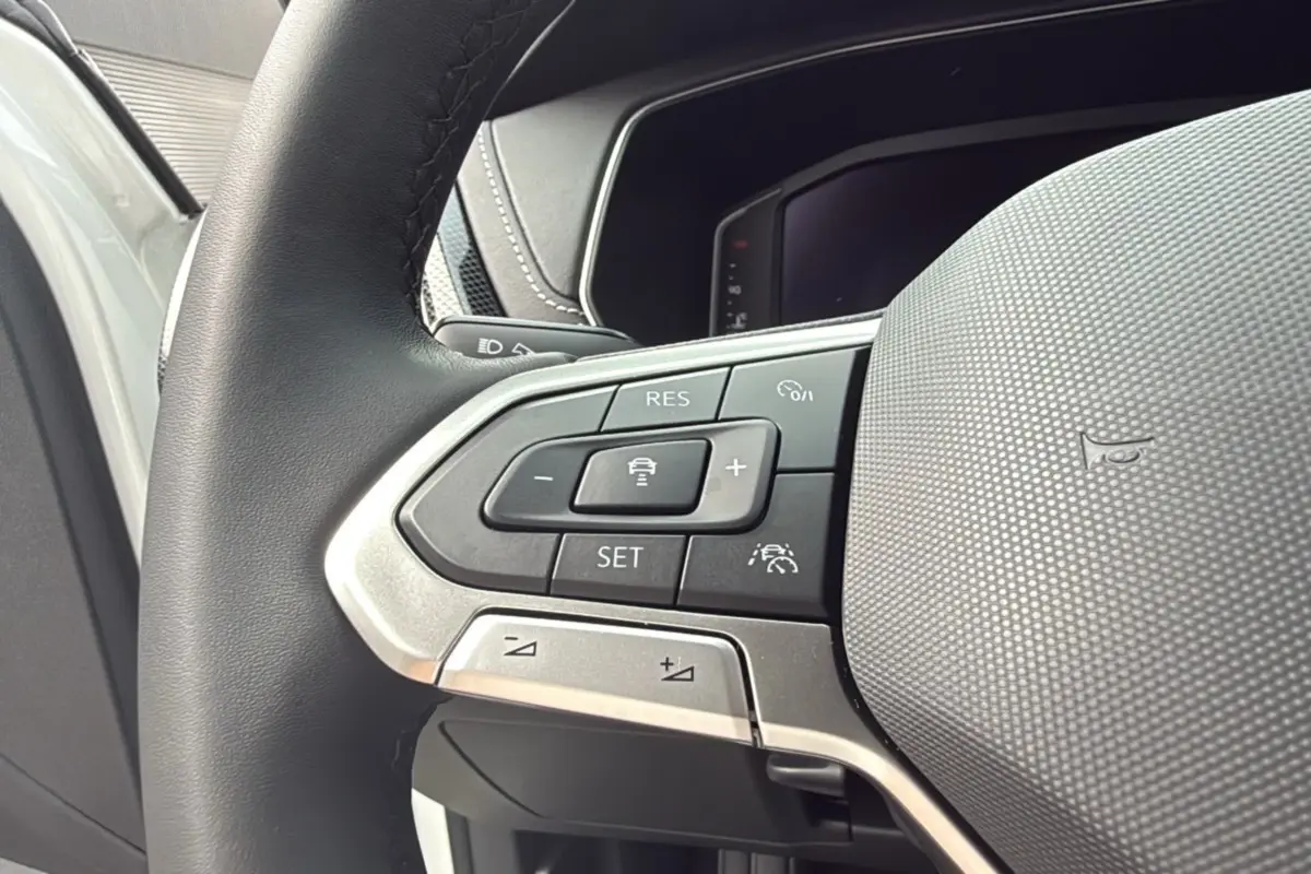 Gros plan sur les commandes multifonctions du volant cuir noir du Volkswagen T-Cross blanc pur 2025.