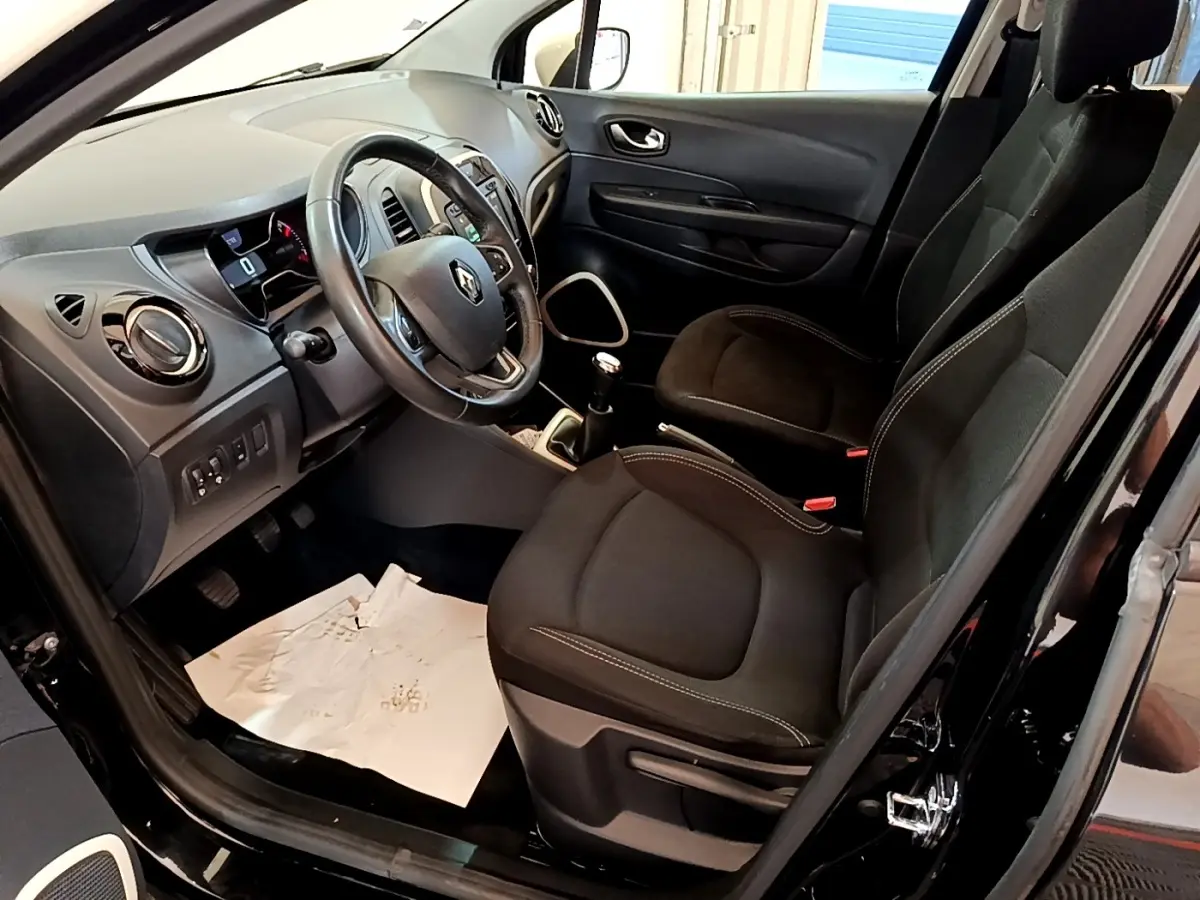 Vue intérieure côté conducteur du Renault Captur Business TCe 90 2018 noir, montrant sièges tissu et tableau de bord avec volant cuir.