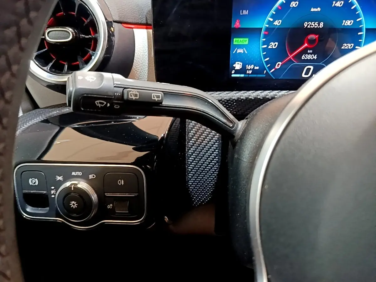 Vue rapprochée du volant cuir et du tableau de bord numérique bleu de la Mercedes Classe A blanche, avec commandes éclairage.