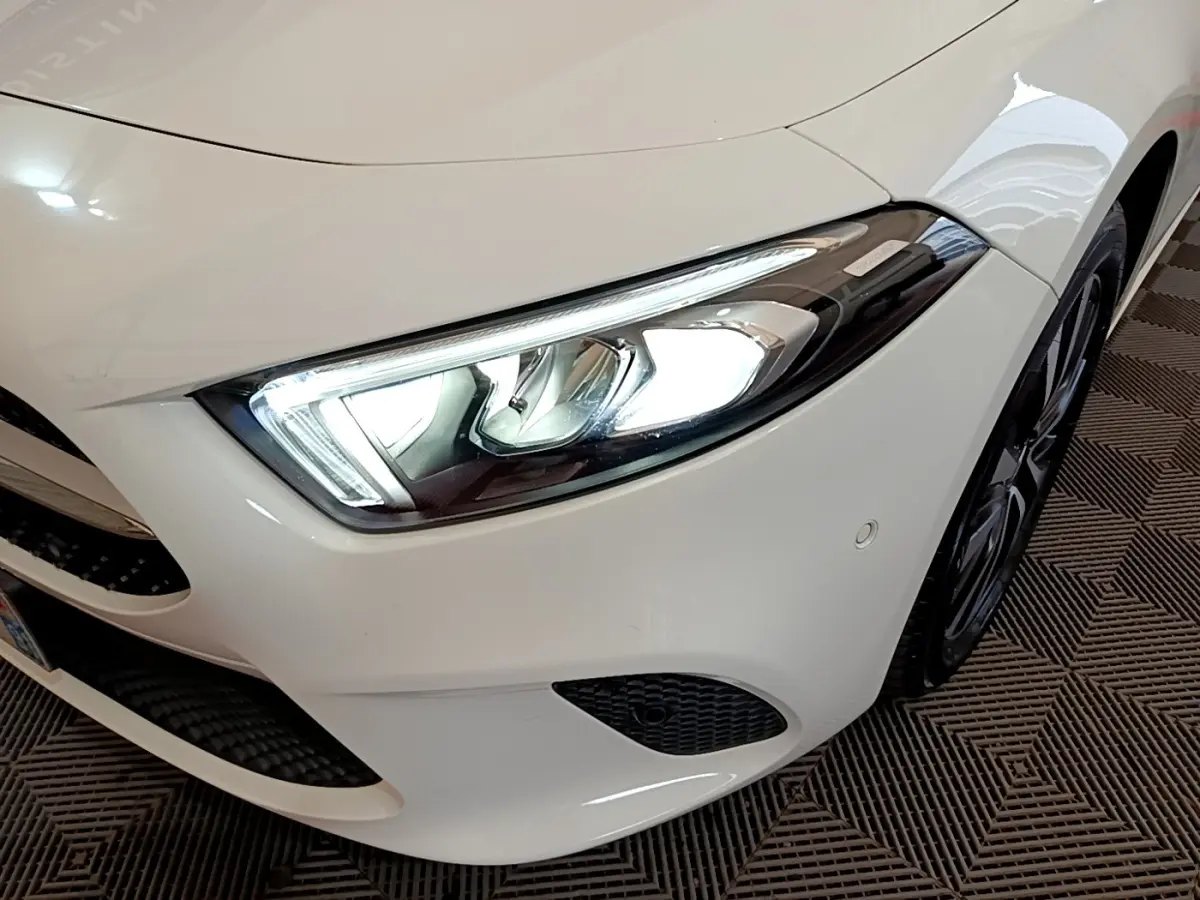 Gros plan sur l'avant droit blanc d'une Mercedes Classe A Berline avec phare LED allumé et jante noire visible.