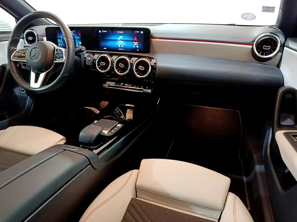 Vue intérieure côté conducteur de la Mercedes Classe A blanche, avec tableau de bord numérique et volant cuir multifonctions.