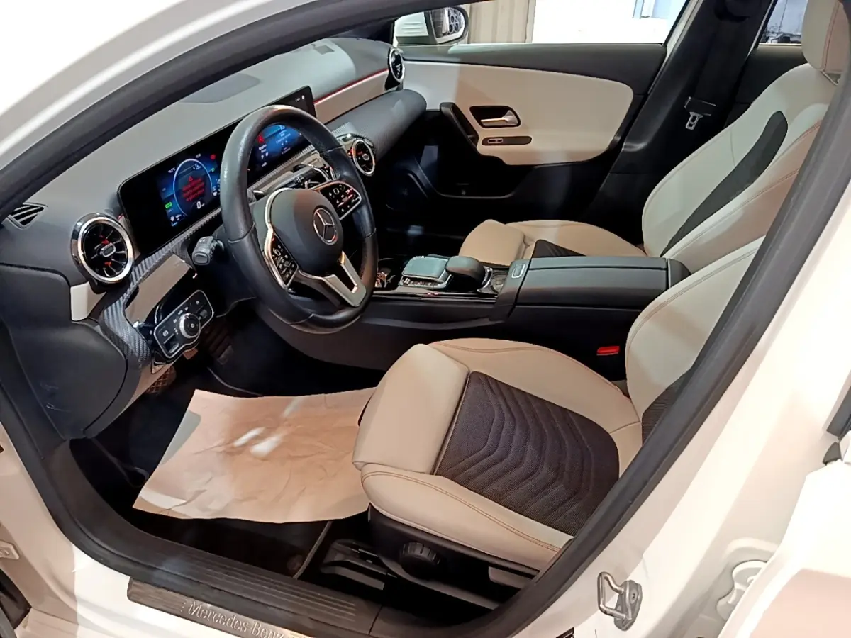 Vue intérieure côté conducteur de la Mercedes Classe A blanche, volant cuir multifonctions et sièges bicolores beige et noir.