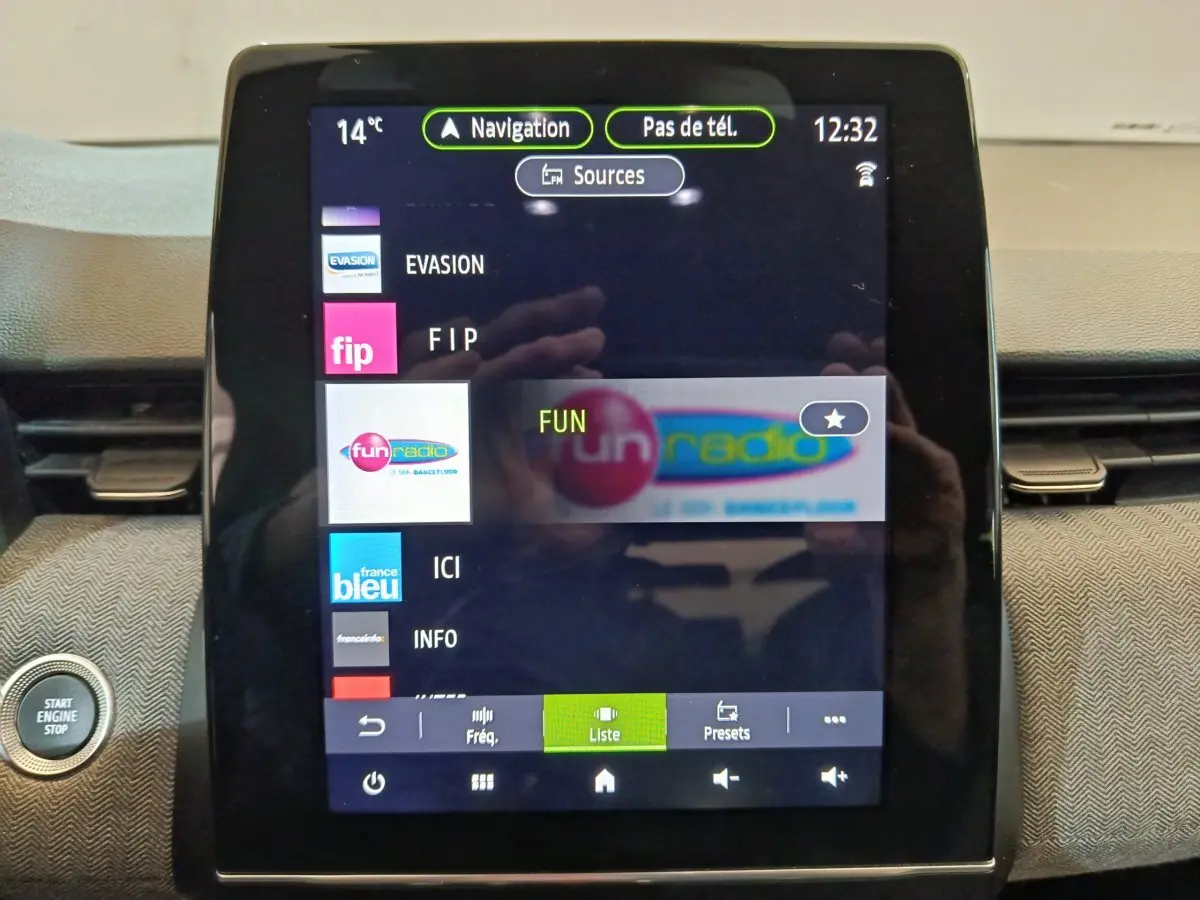 Écran tactile central de la Renault Clio Techno TCe 90 2024 affichant les stations radio avec bouton démarrage visible à gauche.