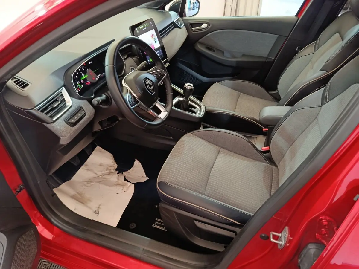 Vue intérieure côté conducteur de la Renault Clio Techno TCe 90 rouge 2024, avec tableau de bord digital et sièges gris.
