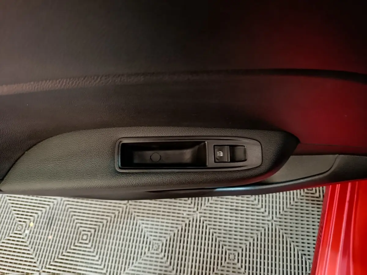 Poignée de porte intérieure côté gauche en plastique noir sur Renault Clio Techno TCe 90 rouge, vue rapprochée.