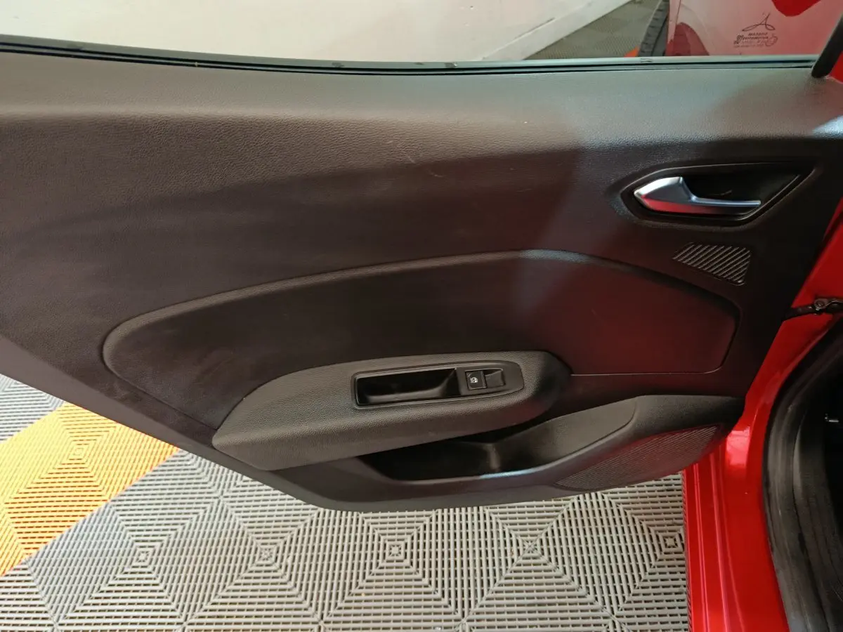 Vue intérieure de la porte avant droite rouge de la Renault Clio 2024 avec poignée et commande de vitre électrique.
