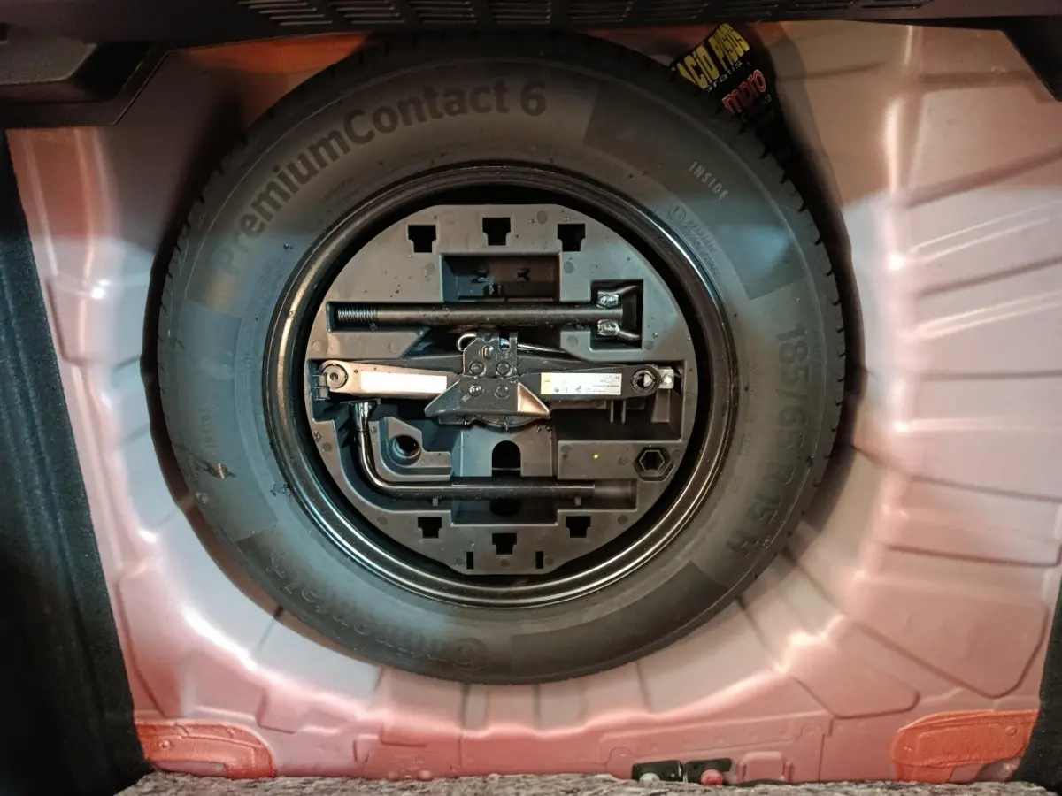 Roue de secours avec outils intégrés dans le coffre d'une Renault Clio rouge 2024, vue de dessus.