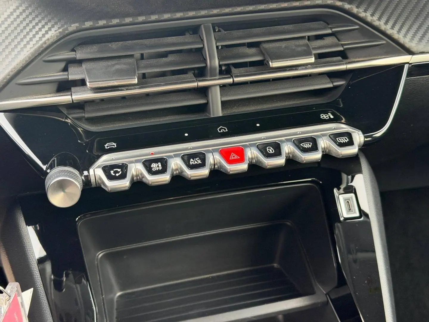 Gros plan sur la console centrale de la Peugeot 208 blanche, montrant les commandes climatisation et bouton rouge de warning.