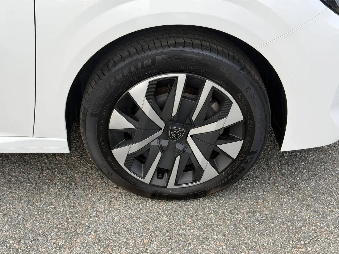 Gros plan sur la roue arrière droite blanche Okénite d'une Peugeot 208 1.2 Hybrid avec jante au design noir et argent.