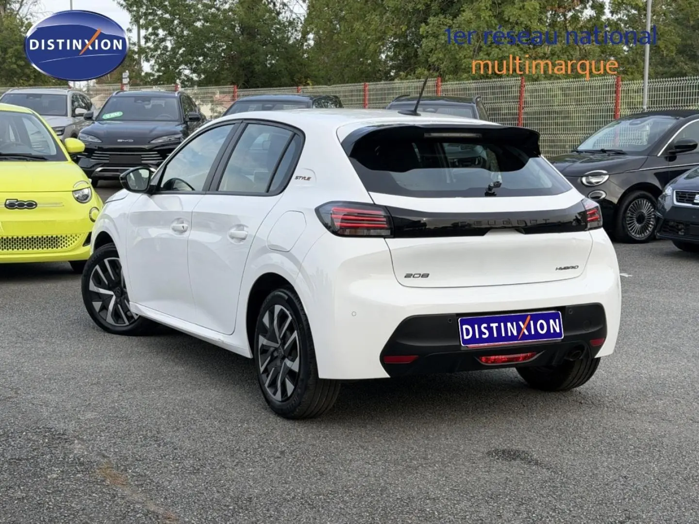 Vue 3/4 arrière droite d'une Peugeot 208 blanche Okénite avec toit noir et jantes distinctives en concession.