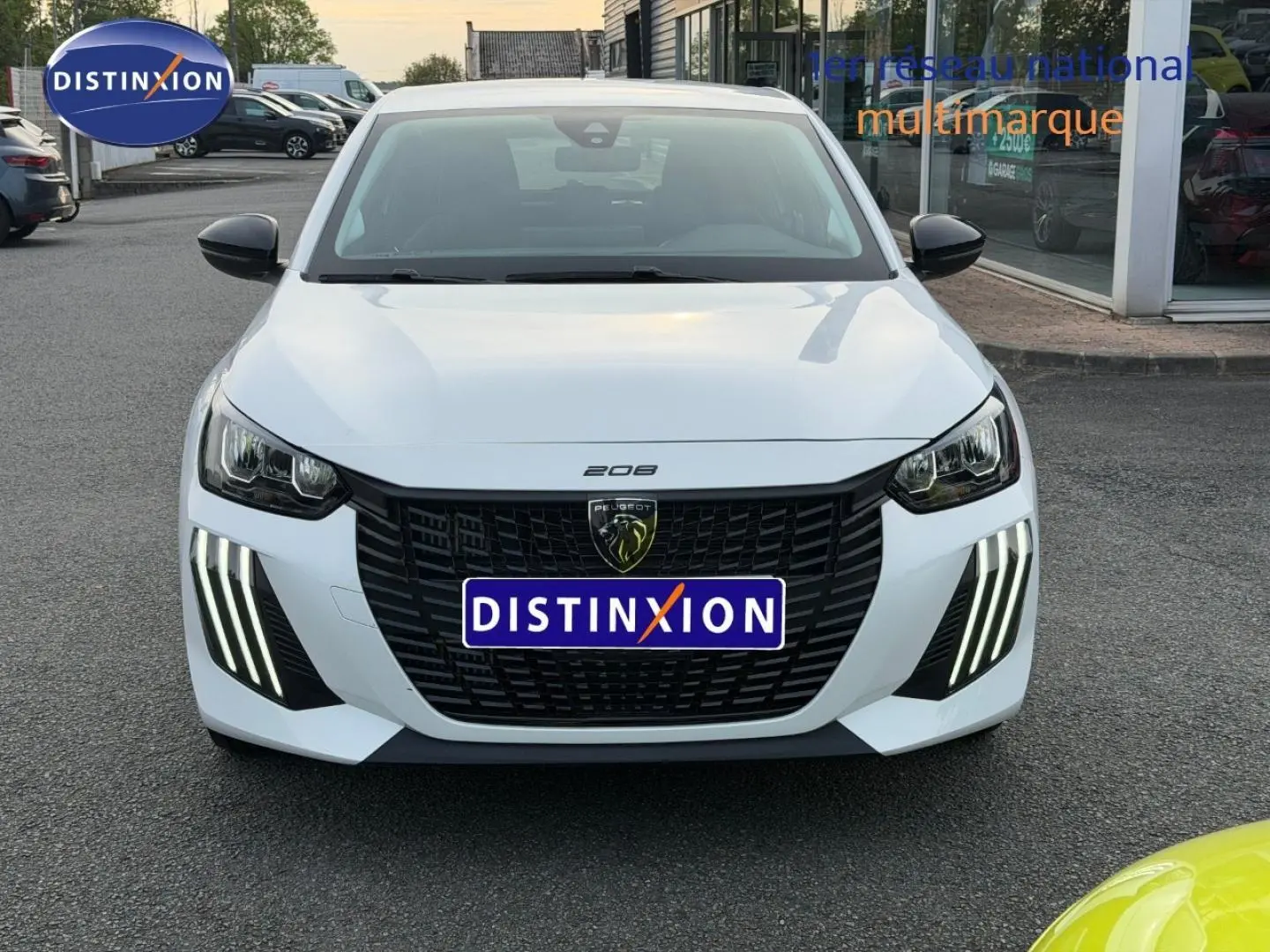 Vue avant d'une Peugeot 208 blanche Okénite avec calandre noire et feux diurnes LED en griffes verticales.