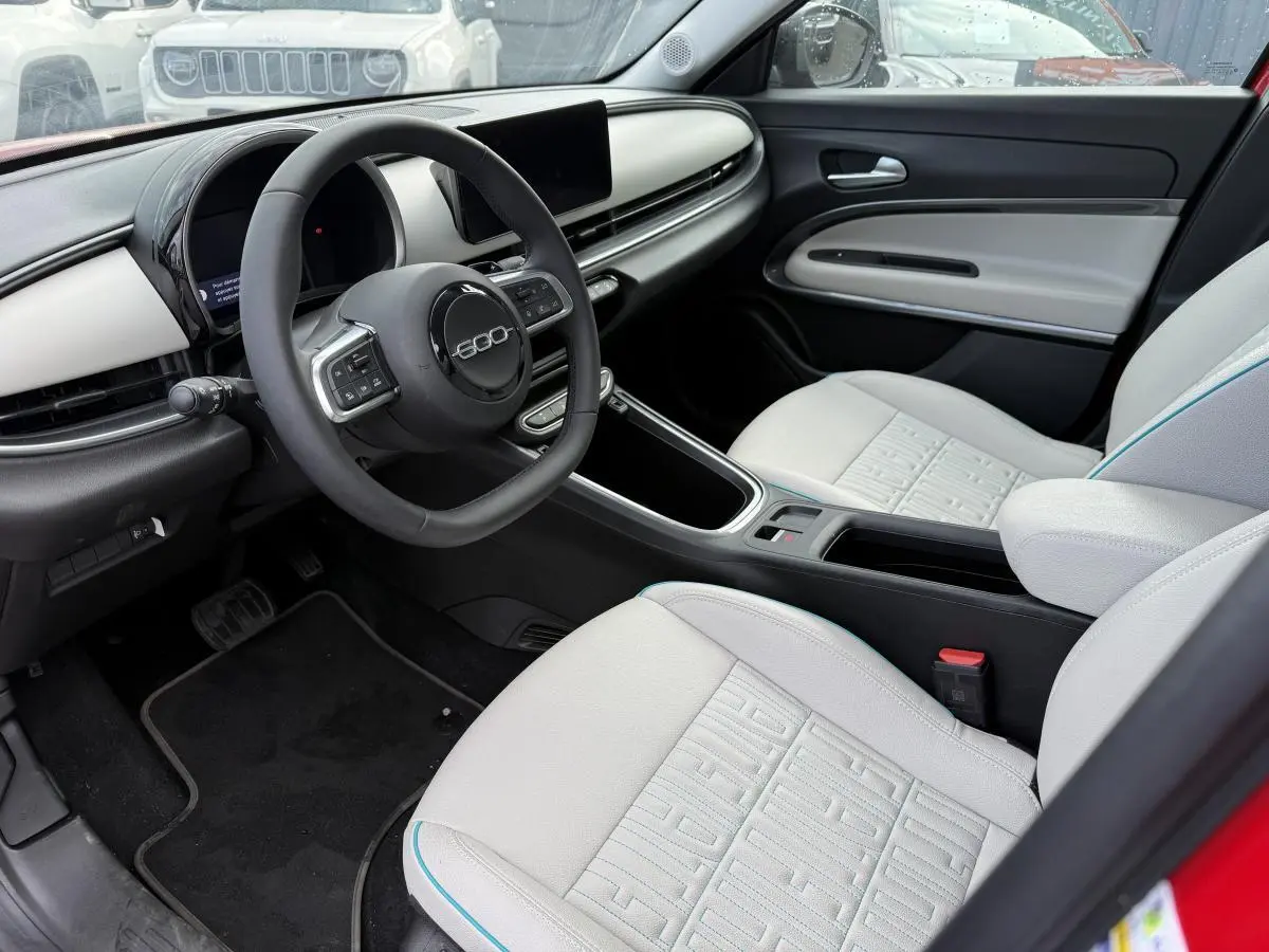 Intérieur avant droit de la FIAT 600 La Prima 2024 rouge, sièges ivoire soft touch avec logo 600 et tableau de bord ivoire.