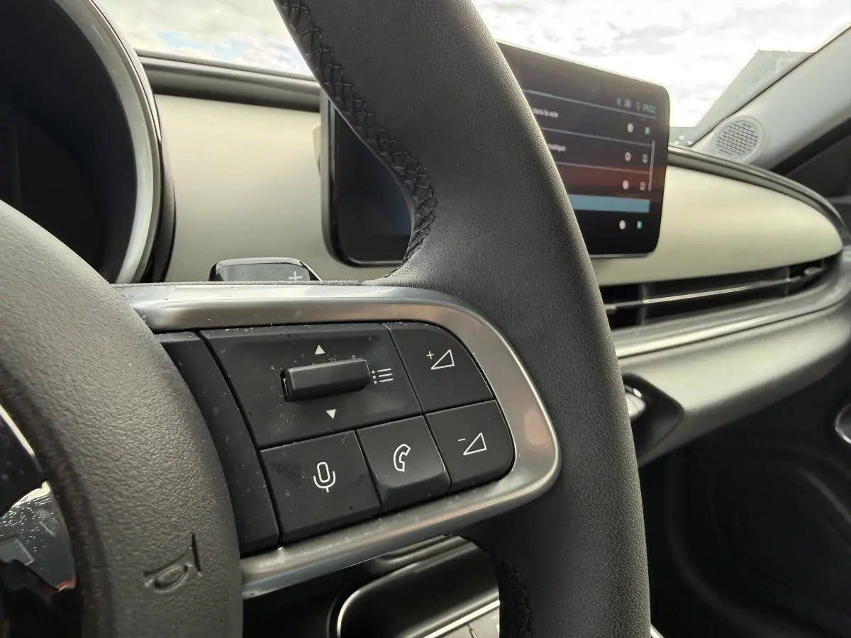 Gros plan sur le volant noir avec commandes intégrées et tableau de bord ivoire de la FIAT 600 rouge 2024 La Prima.