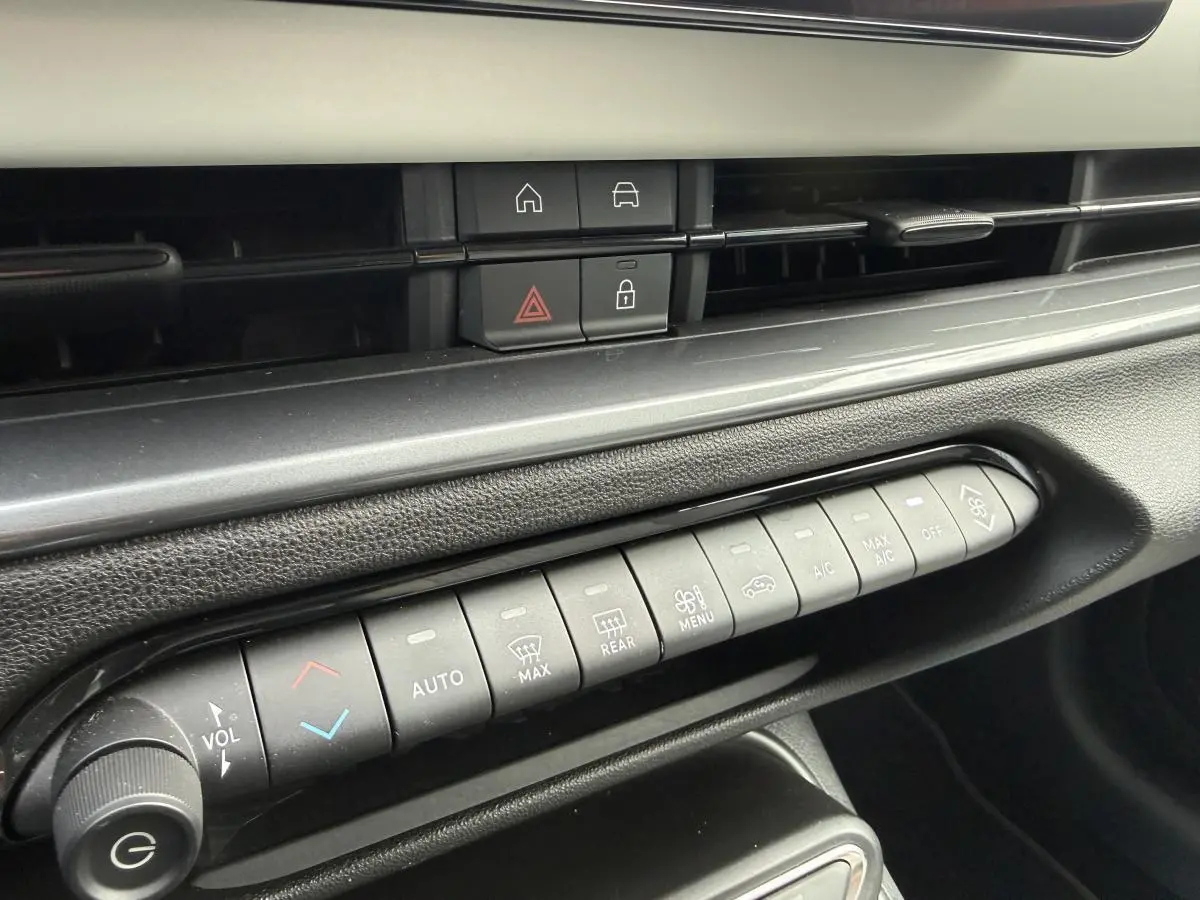 Vue rapprochée de la console centrale noire avec commandes de climatisation et boutons multifonctions sur Fiat 600 rouge 2024