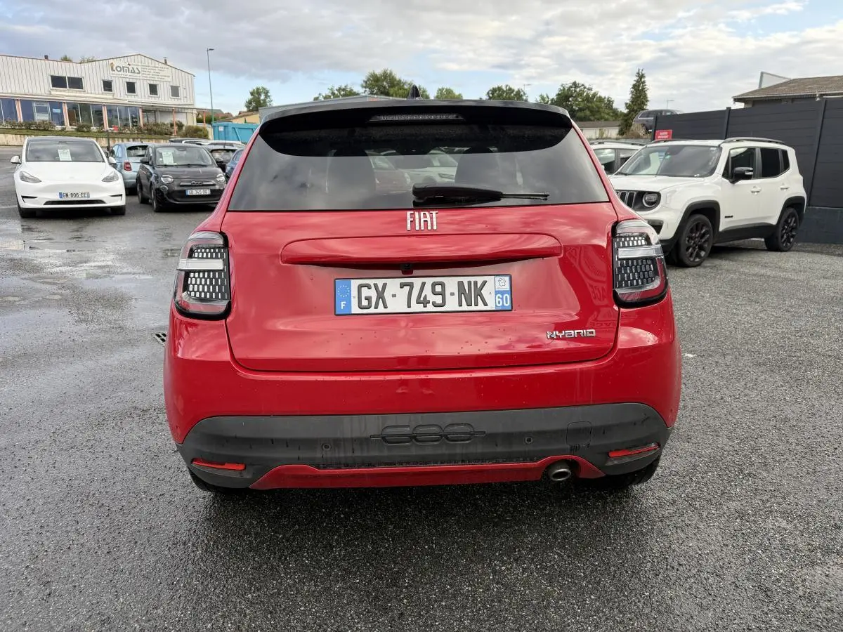 Vue arrière d'une FIAT 600 rouge 2024 avec feux arrière LED et logo Hybrid sur un parking humide.