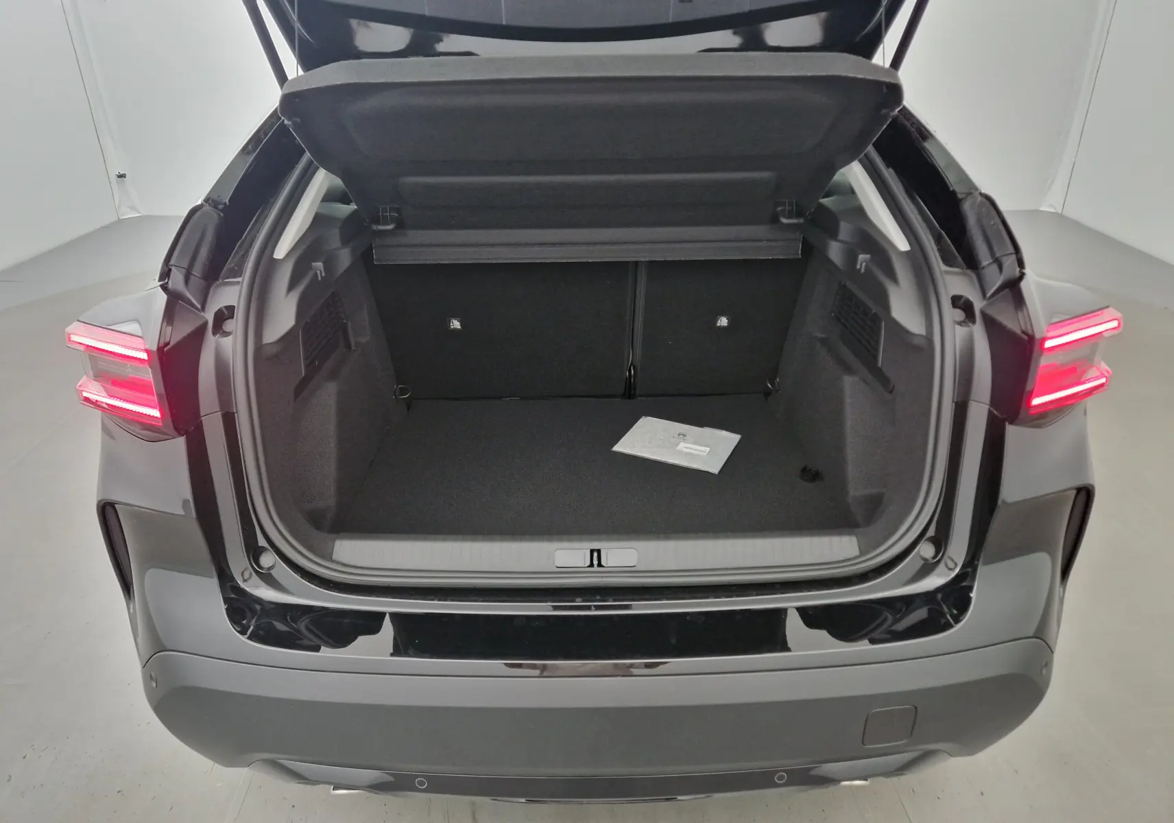 Coffre ouvert vu de l'arrière d'une Citroën C4 noire 2025 avec feux arrière allumés dans un studio blanc.