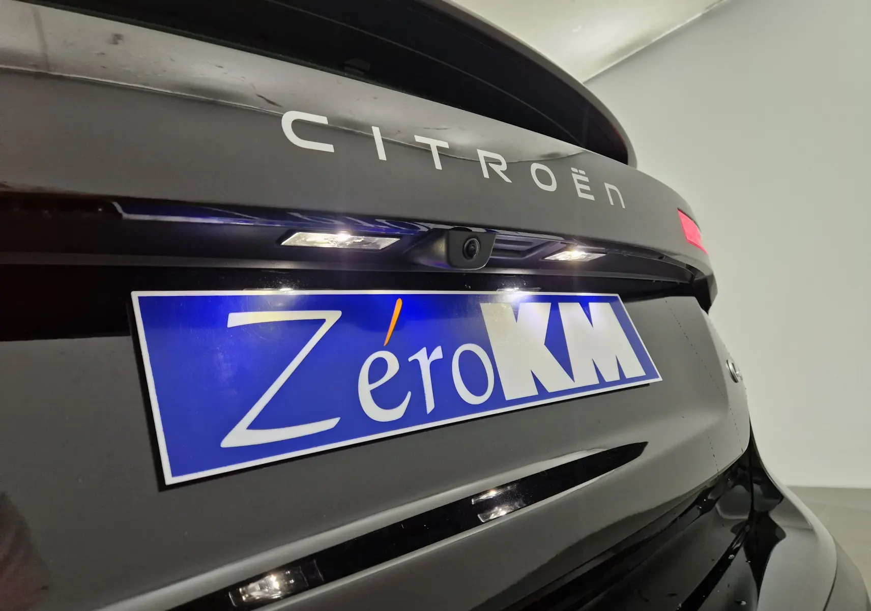 Gros plan sur l'arrière noir brillant d'une Citroën C4 2025 avec caméra de recul et plaque "Zéro KM" bleue.