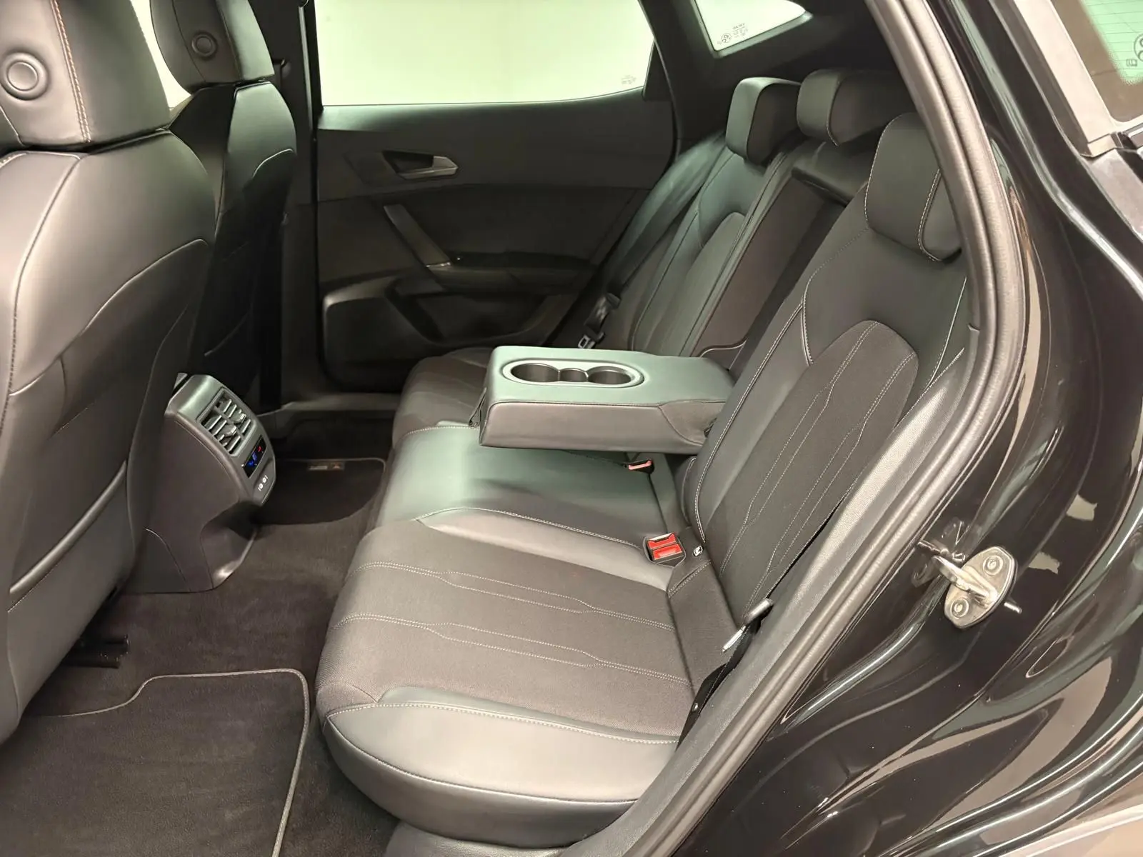 Vue intérieure côté droit des sièges arrière en cuir noir du CUPRA Formentor 2024 avec accoudoir central et porte-gobelets.