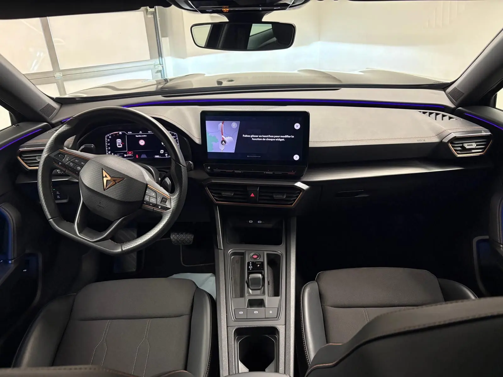 Vue intérieure avant du CUPRA Formentor 1.5 TSI 2024, tableau de bord noir avec éclairage d’ambiance violet et écran tactile central.