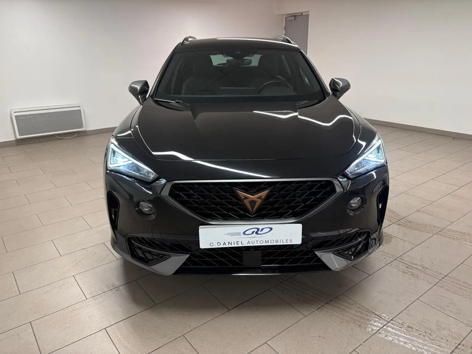 Vue avant d'une CUPRA Formentor 1.5 TSI 150 DSG7 en noir minuit avec phares LED allumés dans un intérieur neutre.