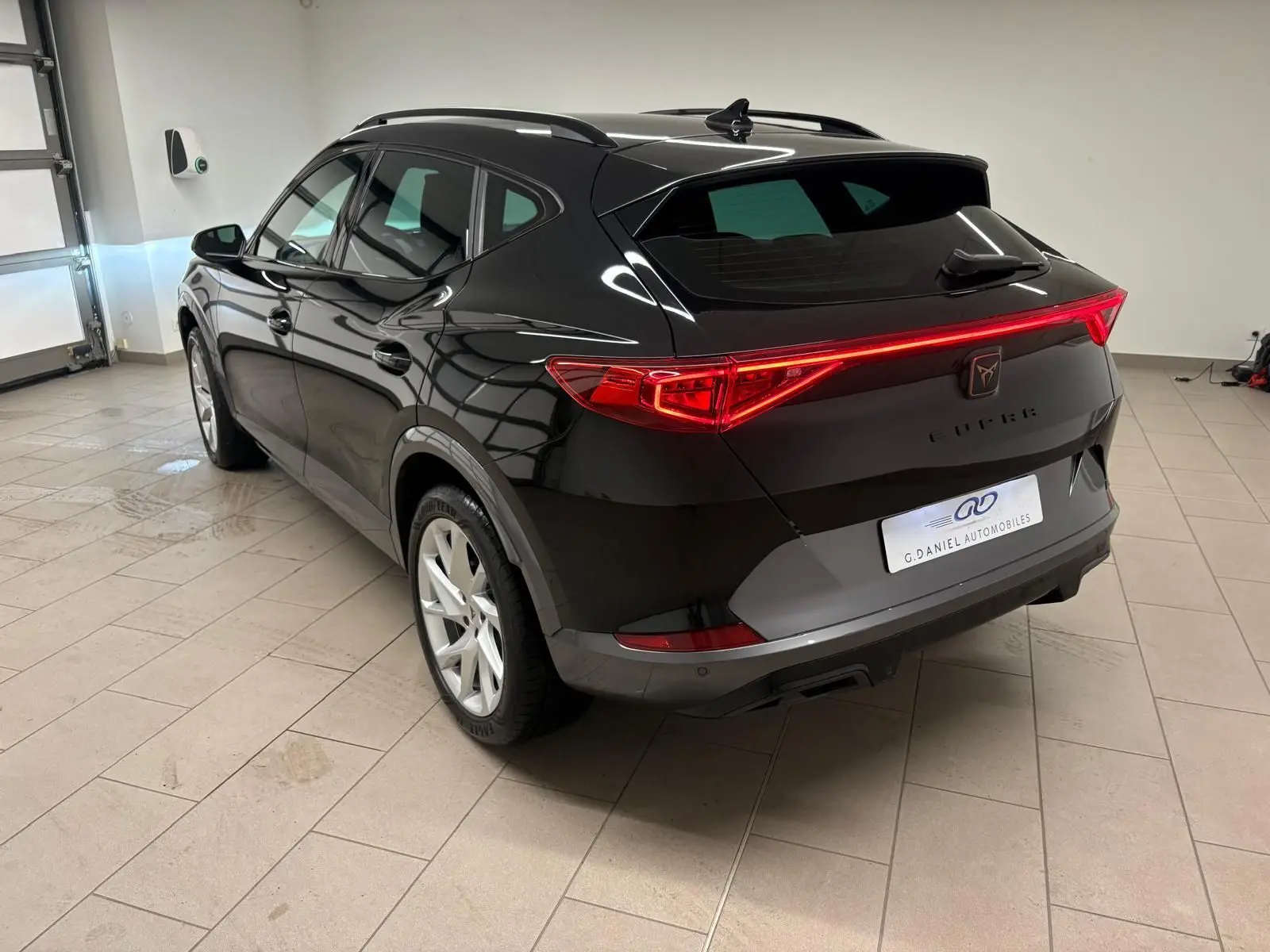 Vue 3/4 arrière droite du CUPRA Formentor noir minuit 2024, avec feux arrière allumés et jantes argentées.