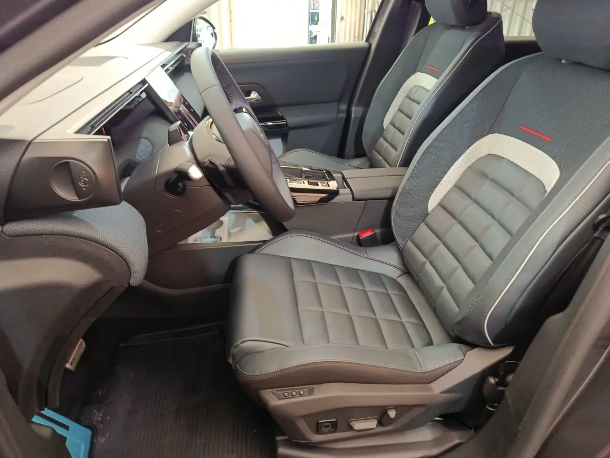 Vue intérieure côté conducteur de la Citroën C5 Hybride 2026 avec sièges cuir gris et détails rouges sur appuie-tête.