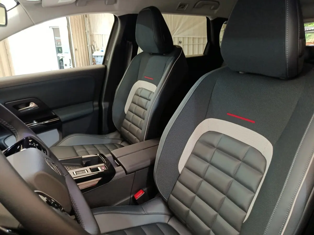 Vue intérieure rapprochée des sièges avant gris foncé et noirs avec surpiqûres rouges de la Citroën C5 Hybride 2026.