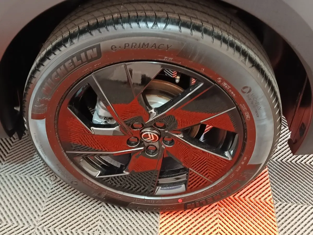 Gros plan sur la roue avant droite d’une Citroën C5 hybride gris foncé avec jante noire brillante et logo Citroën central.