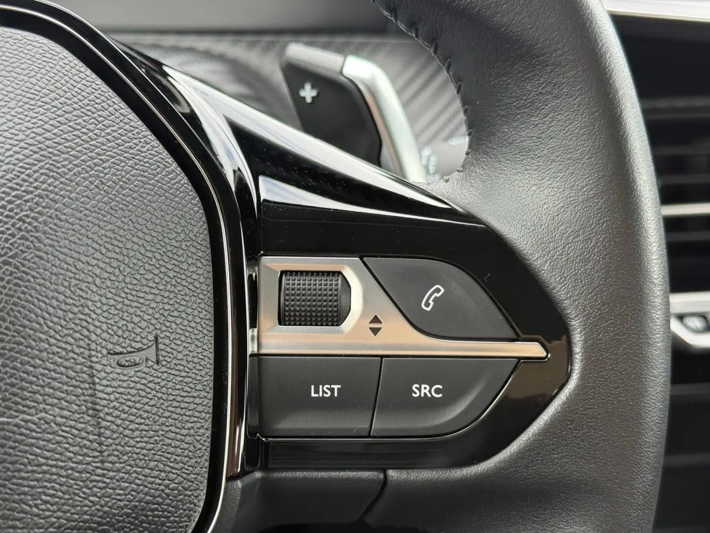 Gros plan sur les commandes noires et argentées au volant du Peugeot 208 noir Perla Nera, avec molette et boutons d’appel.