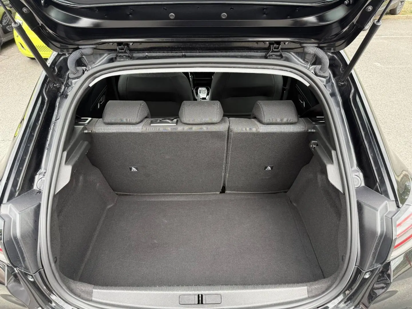 Coffre ouvert vu de l'arrière d'une Peugeot 208 noire Perla Nera avec banquette arrière en tissu gris.