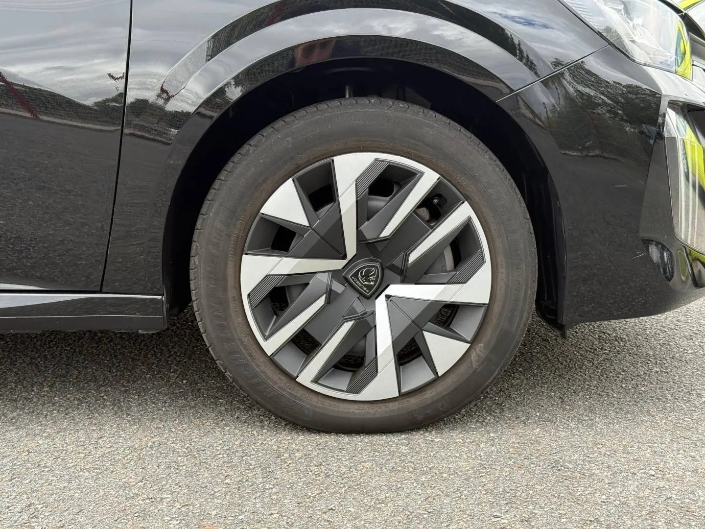 Gros plan sur la roue avant droite d’une Peugeot 208 noire avec jante au design géométrique bicolore.