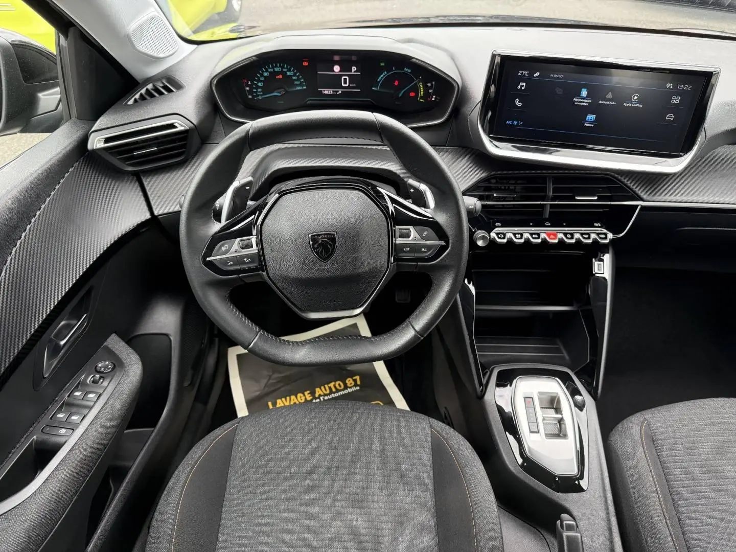 Vue intérieure avant centrée sur le volant noir et le tableau de bord numérique de la Peugeot 208 1.2 Hybrid 2025.