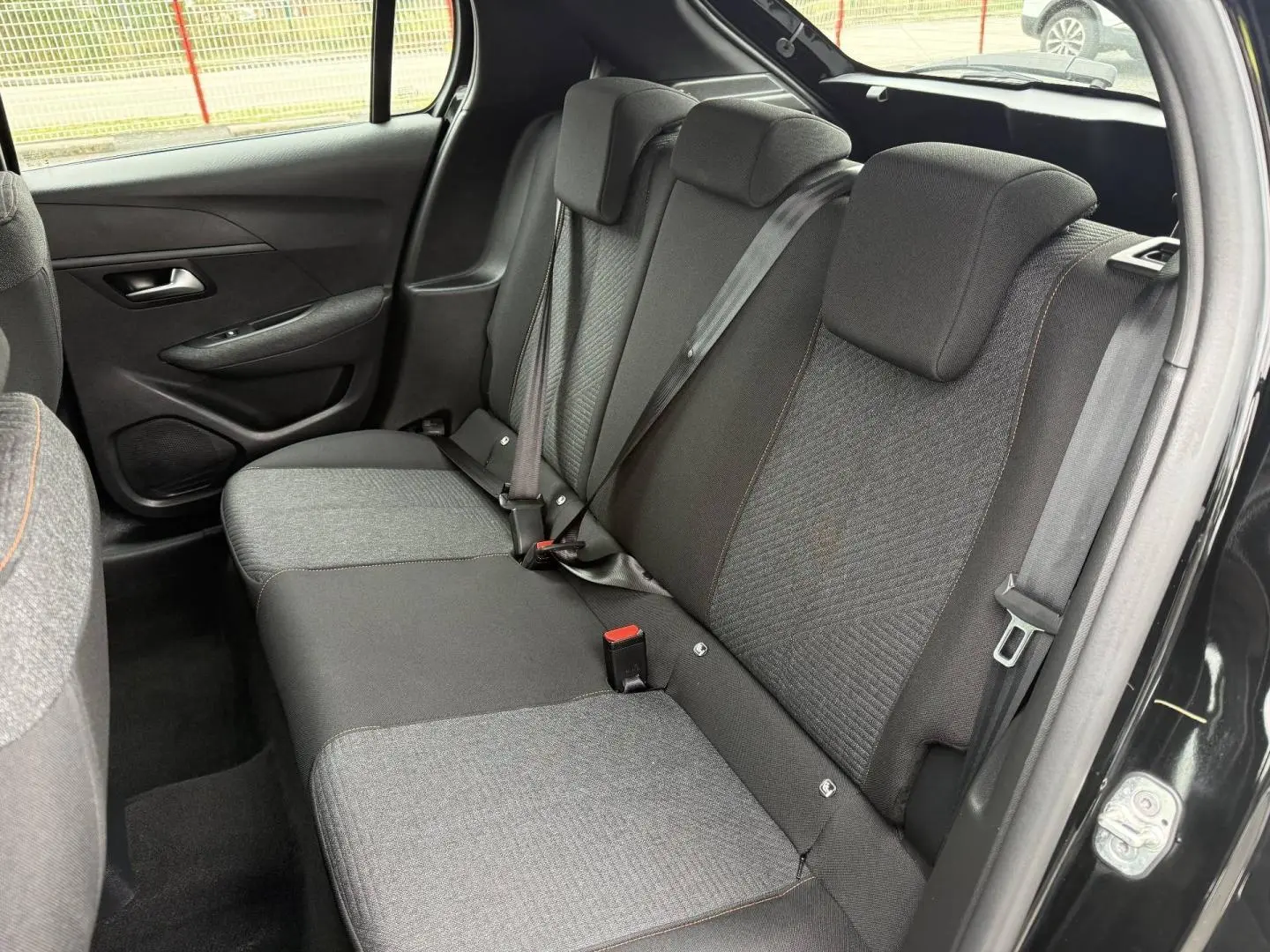 Vue intérieure de la banquette arrière noire et grise avec surpiqûres orange dans une Peugeot 208 2025, porte ouverte côté droit.