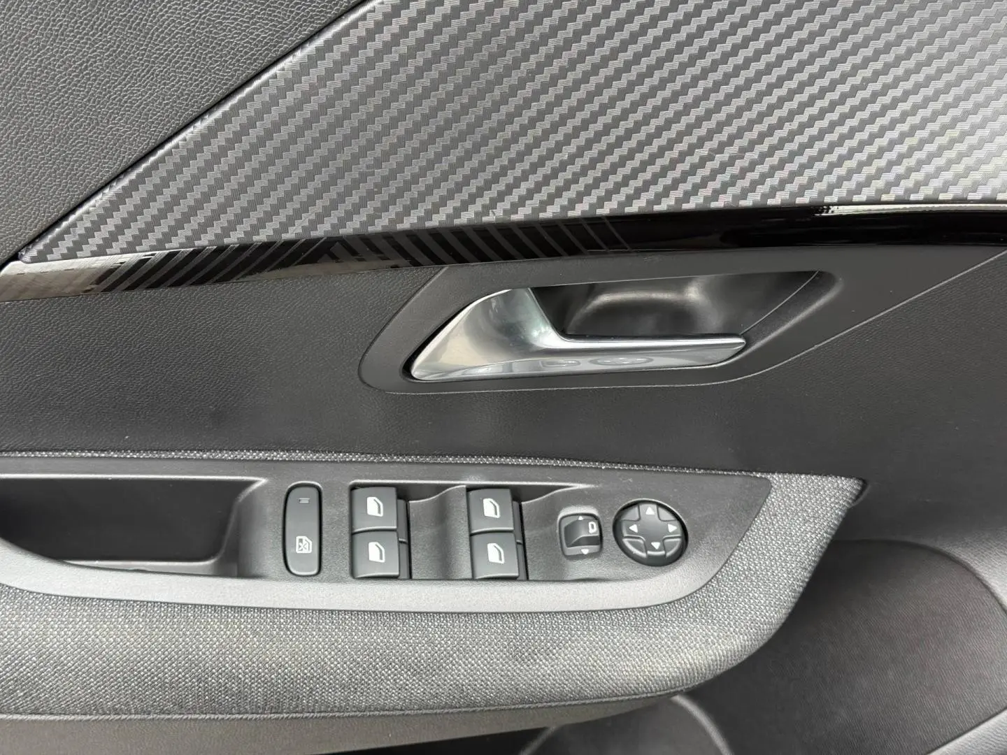 Gros plan sur la porte côté gauche intérieure de la Peugeot 208 1.2 Hybrid noire avec commandes des vitres et poignée argentée.