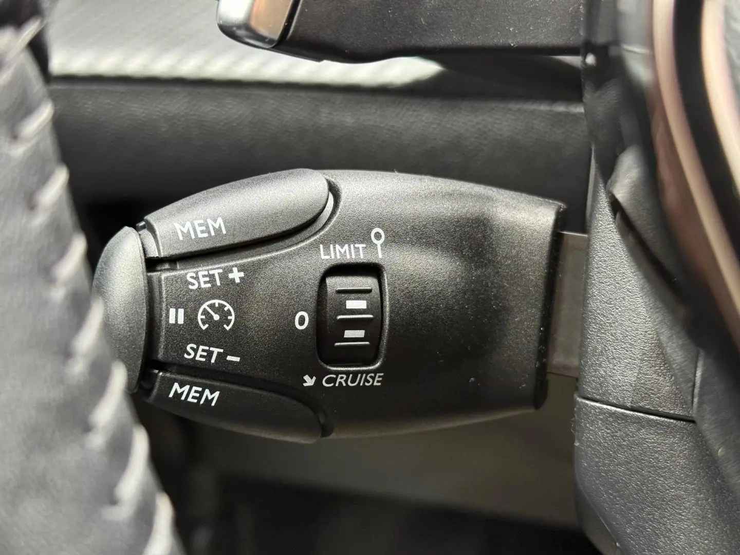 Gros plan sur la commande de régulateur de vitesse noire à gauche du volant dans une Peugeot 208 noire Perla Nera 2025.