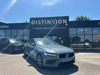 Volvo S60 Thunder Grey Metal vue 3/4 avant garée devant un showroom Distinxion par temps ensoleillé.