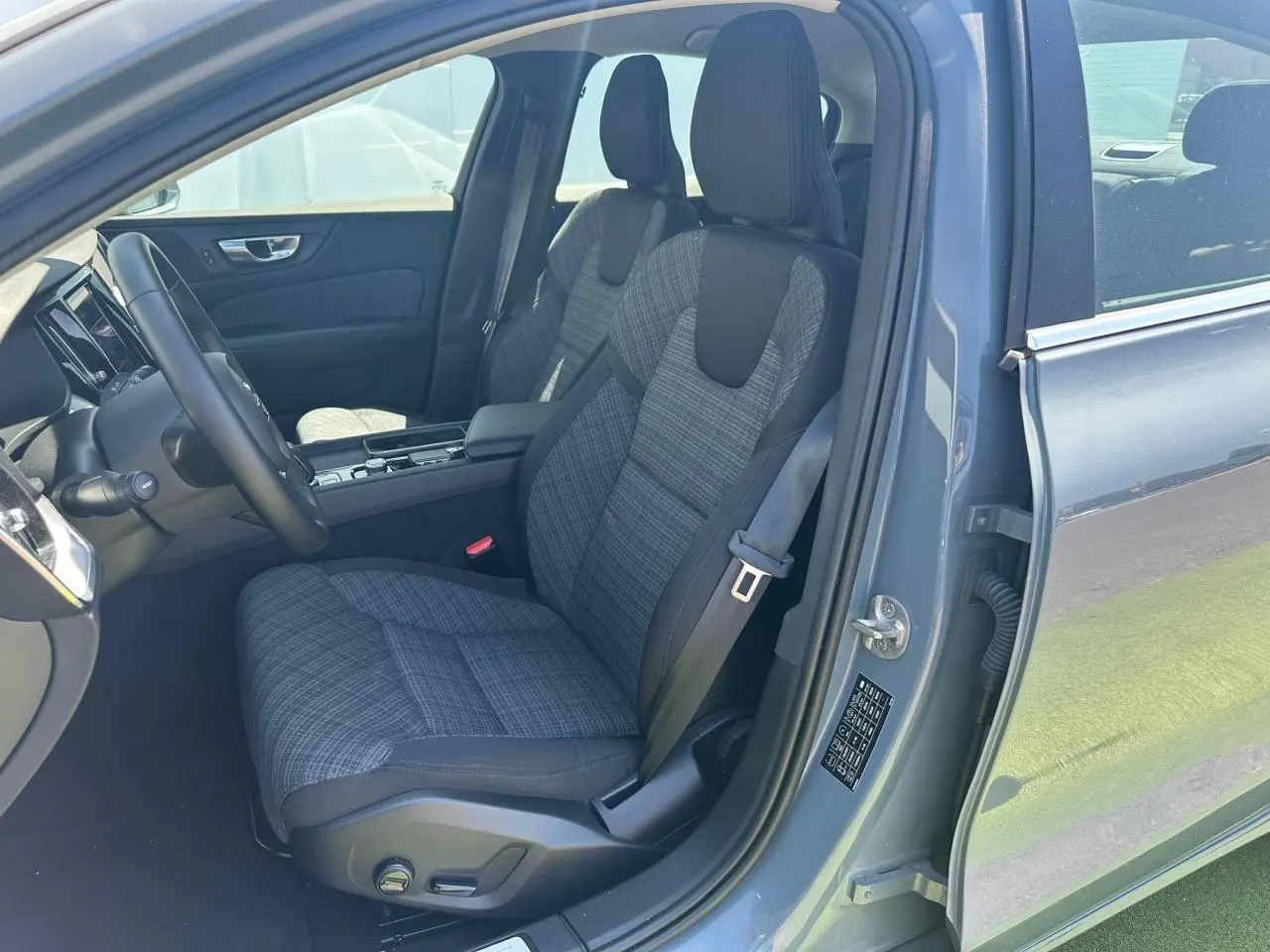 Intérieur avant droit d'une Volvo S60 2024 Thunder Grey Metal, siège tissu gris à motifs et volant noir.