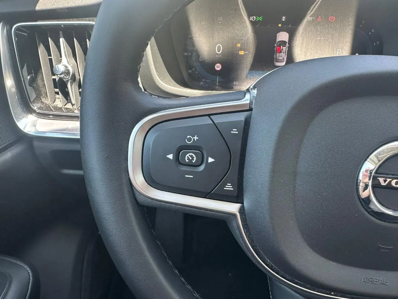 Gros plan sur le volant noir et les commandes de régulateur de vitesse du Volvo S60 2024 en Thunder Grey Metal.