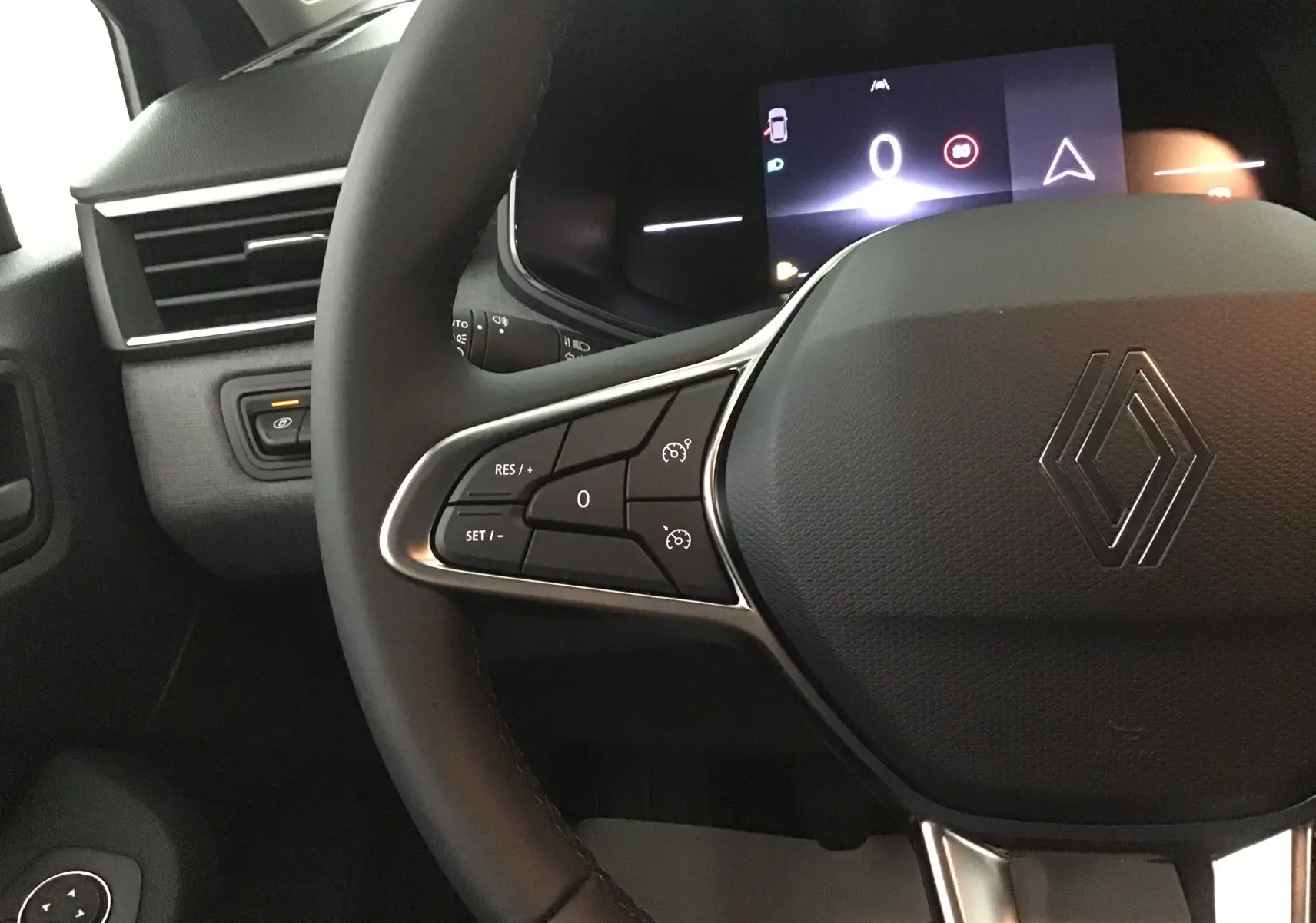 Gros plan sur le volant de la Renault Clio V gris schiste, avec commandes intégrées et tableau de bord digital visible.