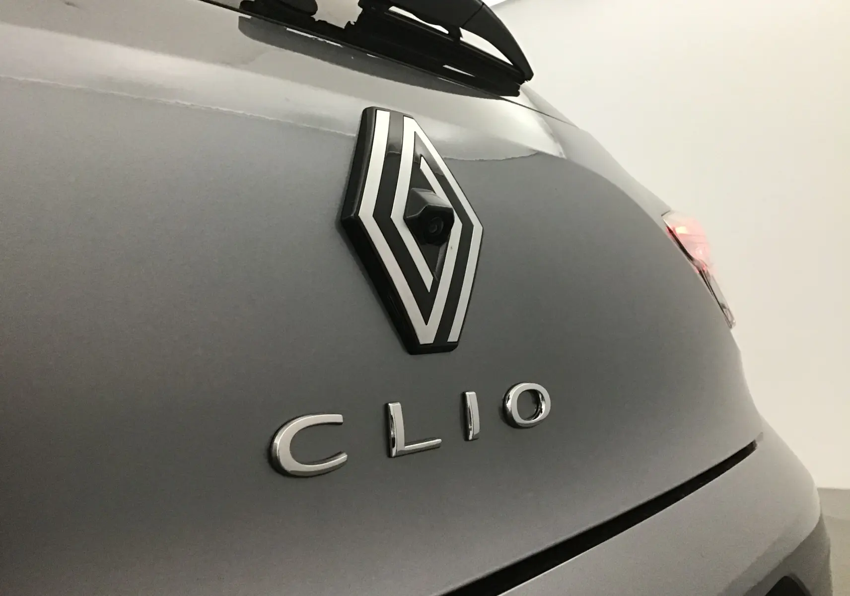 Gros plan sur l'arrière gris schiste d'une Renault Clio V mettant en valeur le logo et la caméra de recul intégrée.