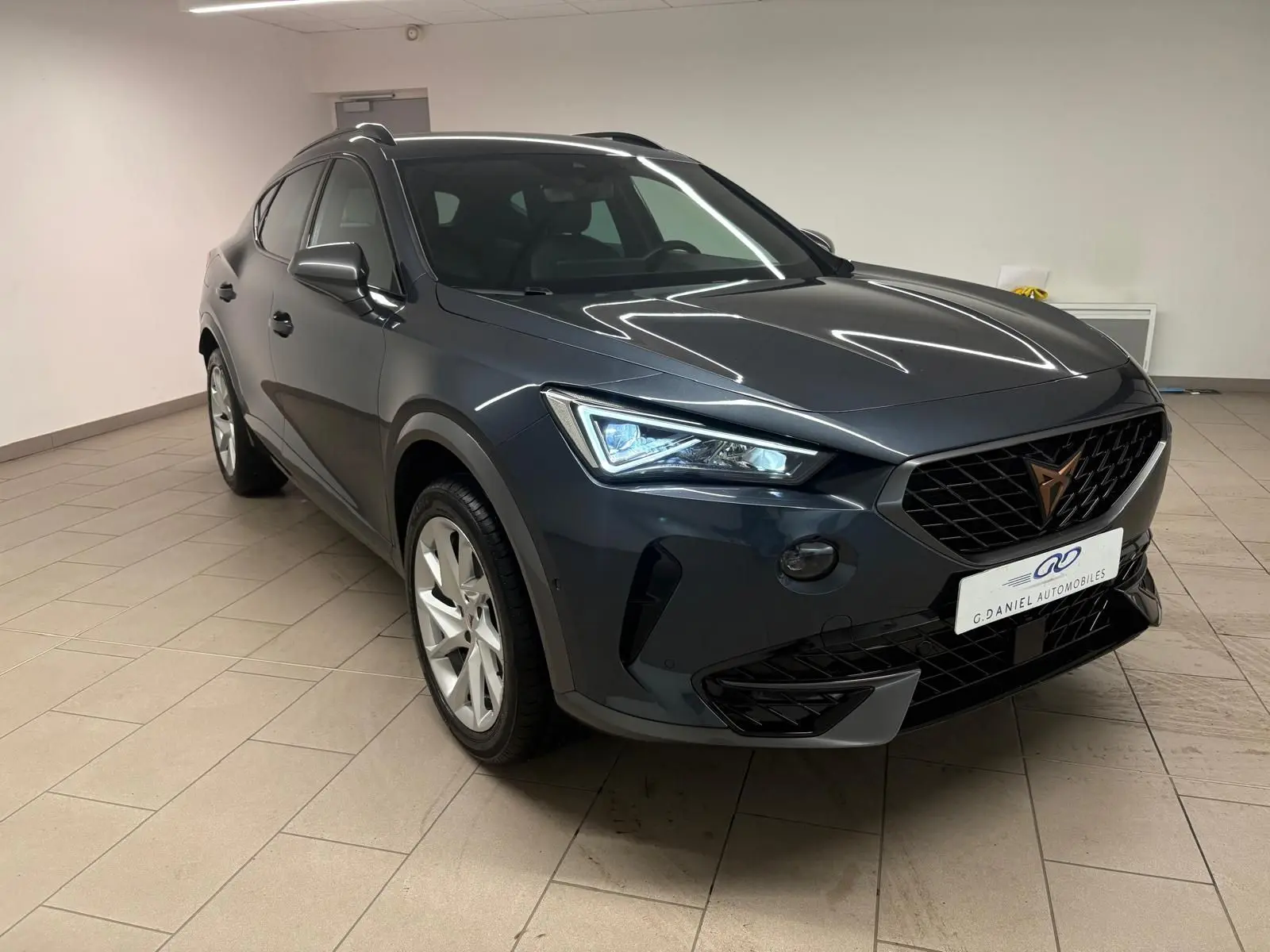 Vue 3/4 avant du CUPRA Formentor 1.5 TSI 150 DSG7 en gris magnétique, avec calandre noire et phares LED allumés.