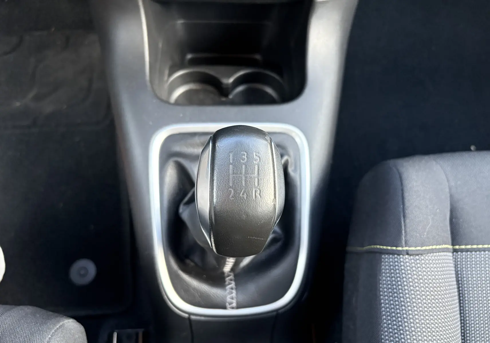 Le levier de vitesses manuel noir de la Citroën C3 rouge, vu de dessus au centre de l'habitacle.