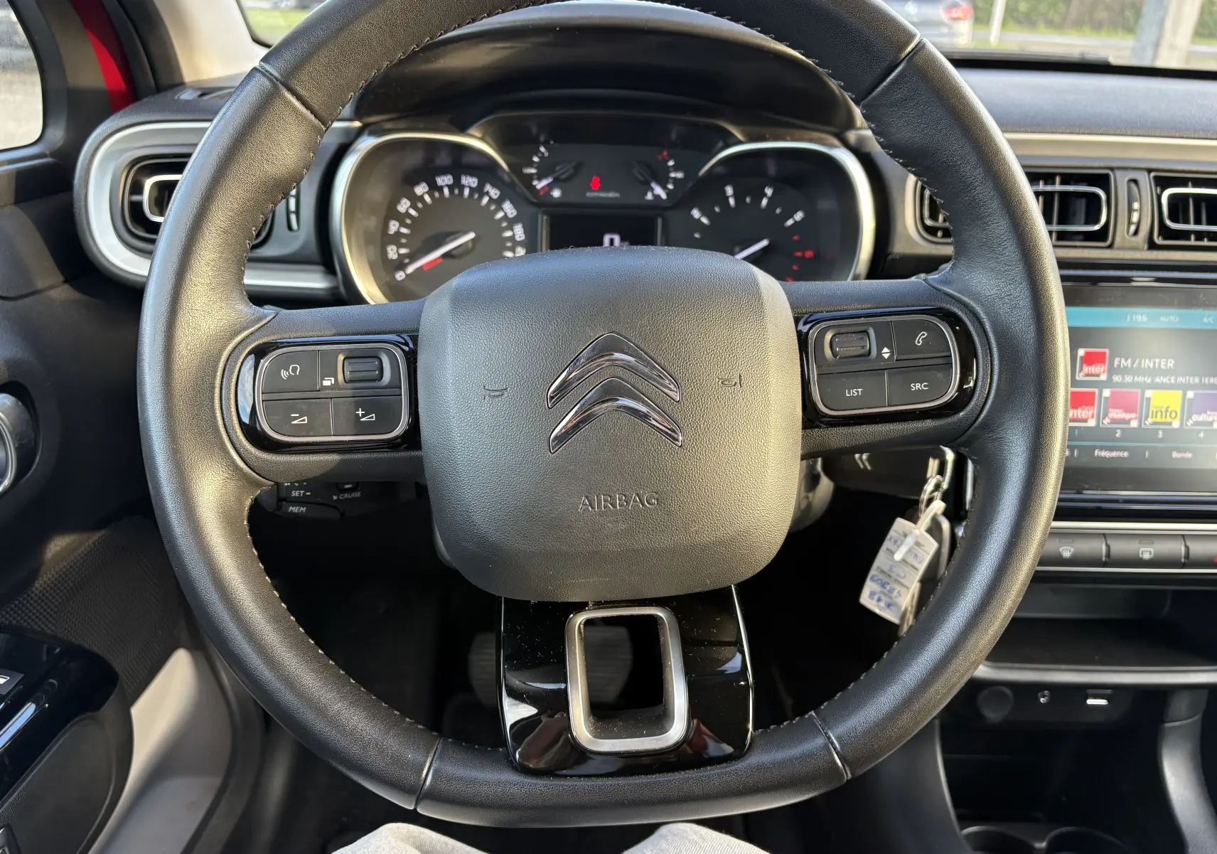 Vue intérieure centrée sur le volant noir de la Citroën C3 rouge, avec tableau de bord et écran multimédia visibles.