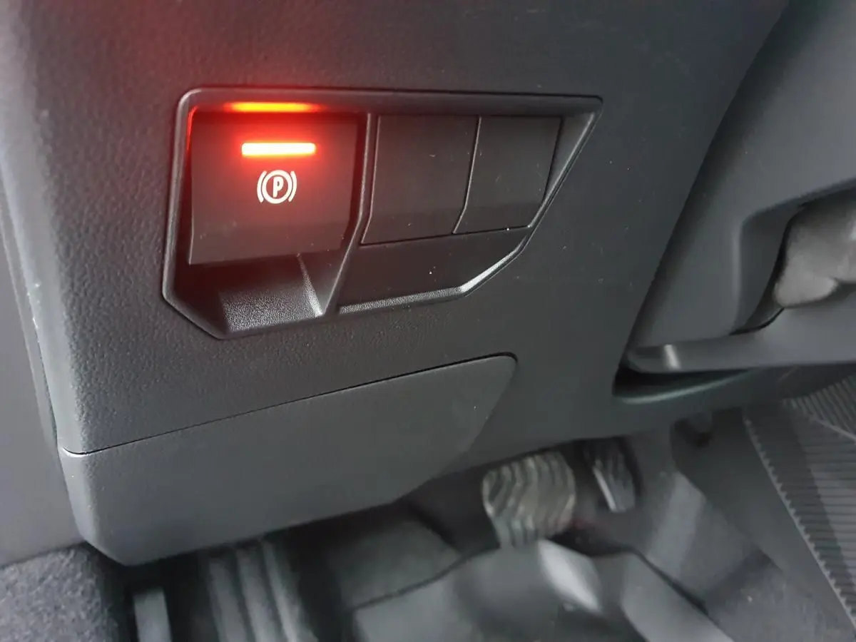 Gros plan sur le bouton de frein à main électronique allumé dans l'habitacle noir du Dacia Duster blanc glacier 2025.
