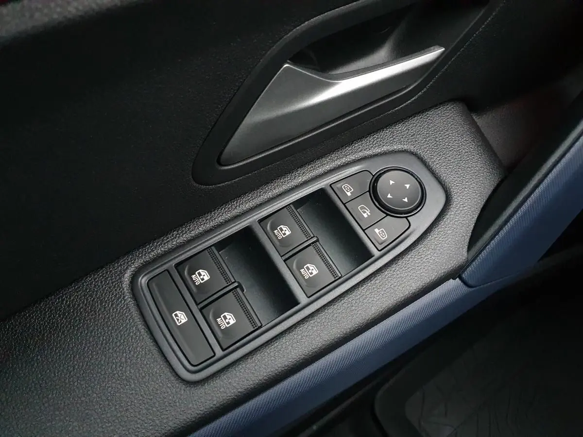 Gros plan sur les commandes de lève-vitres et rétroviseurs côté conducteur du Dacia Duster blanc glacier 2025.