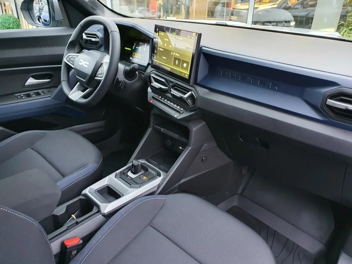 Vue intérieure côté conducteur du tableau de bord du Dacia Duster 1.6 Hybrid 140 blanc glacier avec écran tactile et volant multifonction.