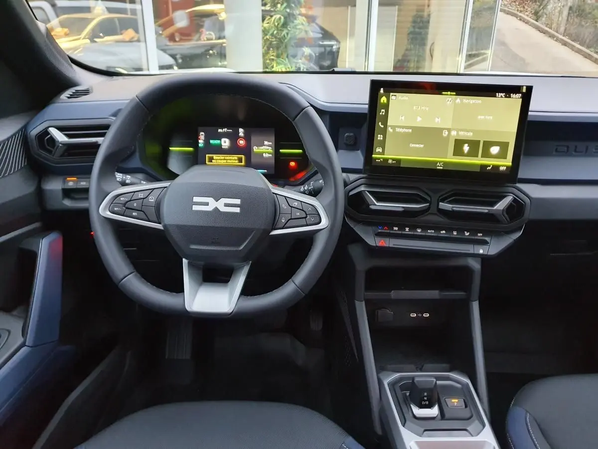 Vue intérieure frontale du tableau de bord du Dacia Duster blanc glacier, avec écran tactile et volant multifonction.