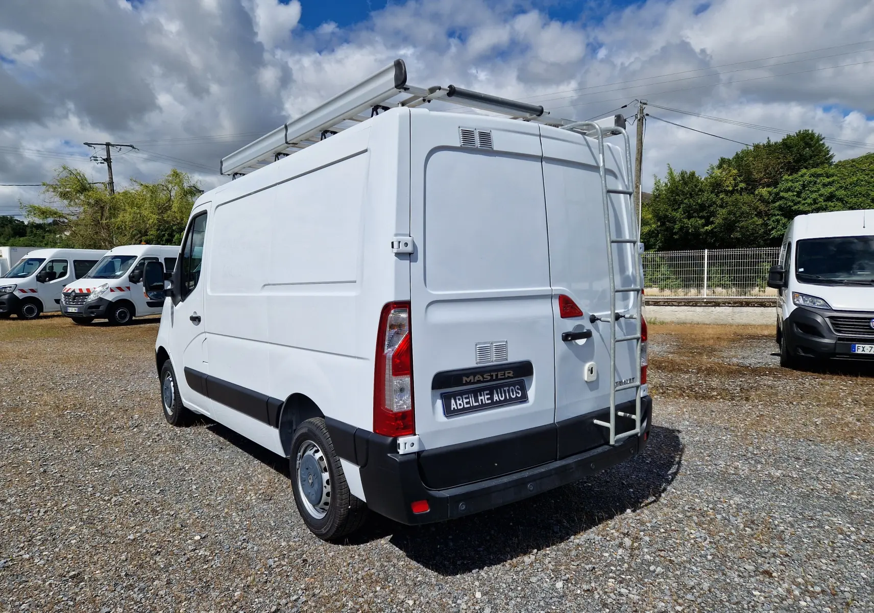 Vue 3/4 arrière droite d’un utilitaire blanc Renault Master 2019 avec galerie et échelle sur porte arrière.